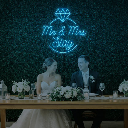 Photo of the 'Mr & Mrs EST' neon sign glowing in ice blue against a styled interior wall.