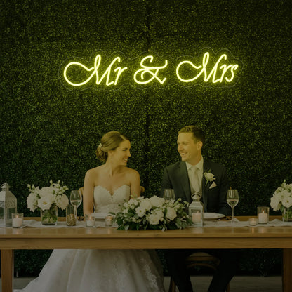 Photo of the 'Mr & Mrs' neon sign glowing in lemon yellow against a styled interior wall.