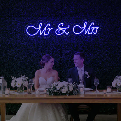 Photo of the 'Mr & Mrs' neon sign glowing in deep blue against a styled interior wall.