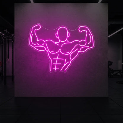 'Muscle Man (Torso-Up Flex)' neon sign glowing in light pink against a styled interior wall.