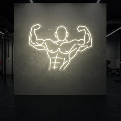  'Muscle Man (Torso-Up Flex)' neon sign glowing in warm white against a styled interior wall.