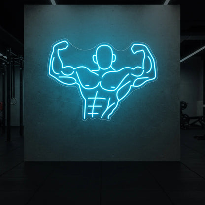 'Muscle Man (Torso-Up Flex)' neon sign glowing in ice blue against a styled interior wall.
