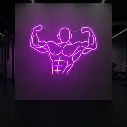  'Muscle Man (Torso-Up Flex)' neon sign glowing in deep pink against a styled interior wall.
