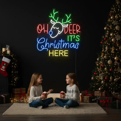 Photo of the 'Oh Deer It's Christmas Here' neon sign glowing in cool white against a styled interior wall.