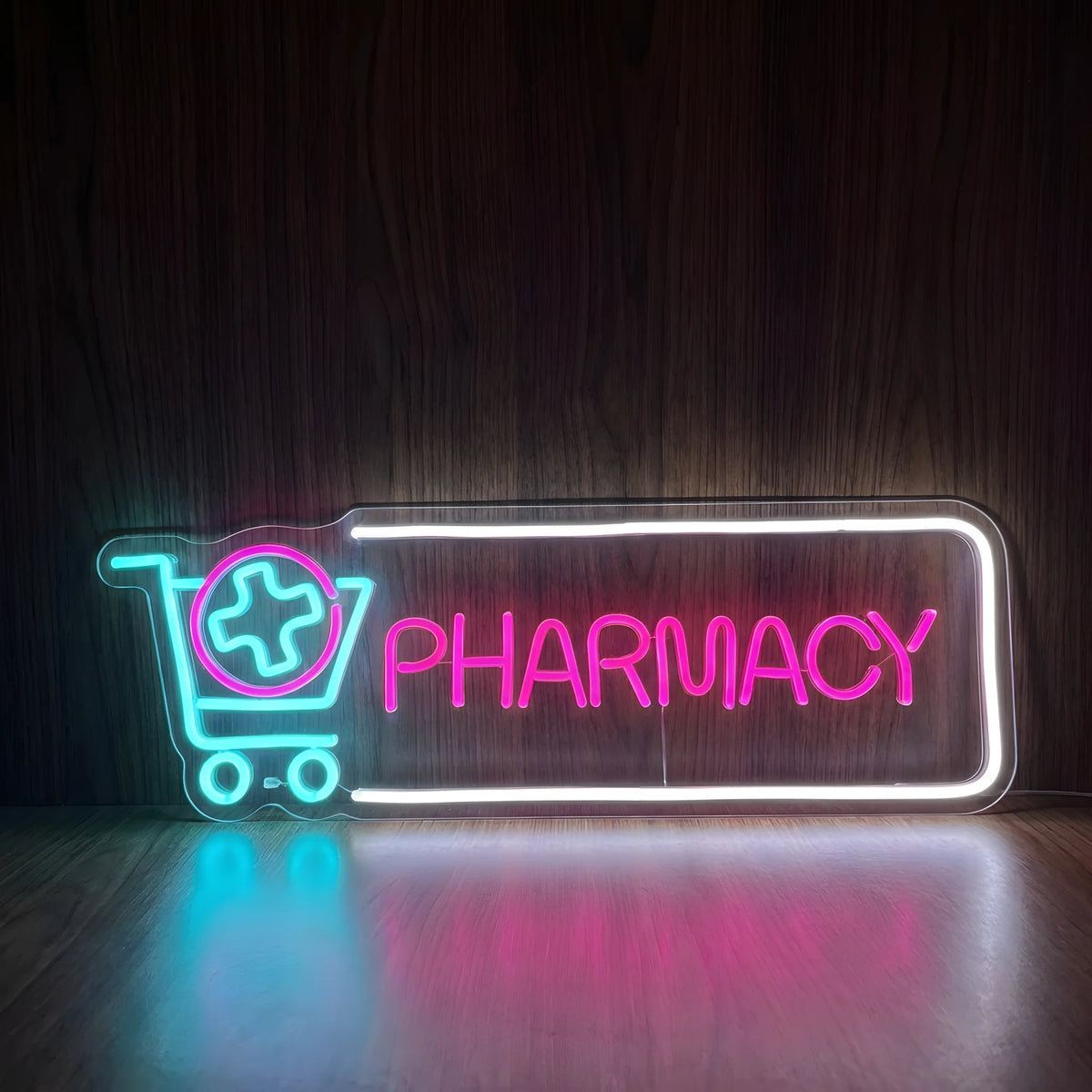 Pharmacy Shopping Cart LED neon sign featuring a cyan-blue shopping cart with a pink circular medical cross beside bright pink PHARMACY lettering inside a cool white rectangular border on clear acrylic backing.
