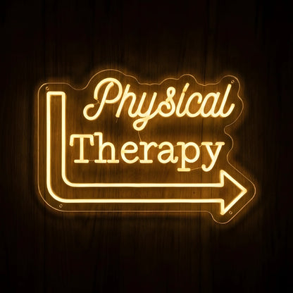 Physical Therapy Direction Arrow LED Neon Sign featuring warm yellow Physical Therapy lettering and a right-pointing arrow on clear cut-to-shape acrylic against a dark wooden wall.