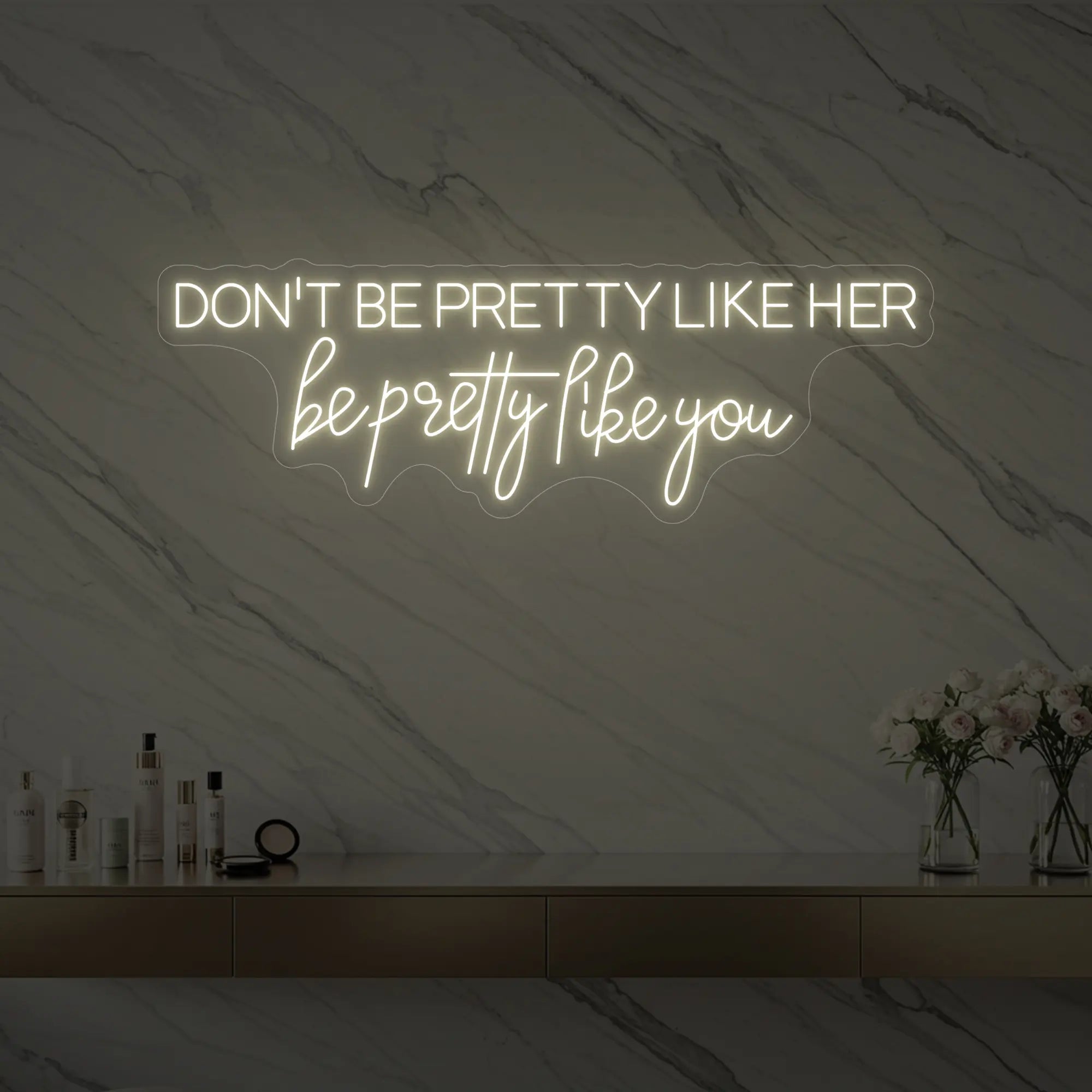 Photo of the 'DON'T BE PRETTY LIKE HER — be pretty like you' neon sign glowing in warm white against a styled interior wall.