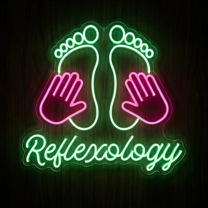 Reflexology Footprints LED Neon Sign featuring green glowing footprints, pink massage hands, and green Reflexology script lettering on clear acrylic backing against a dark wooden wall.