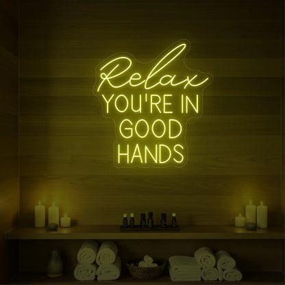 Photo of the 'Relax You're in Good Hands' neon sign glowing in lemon yellow against a styled interior wall.