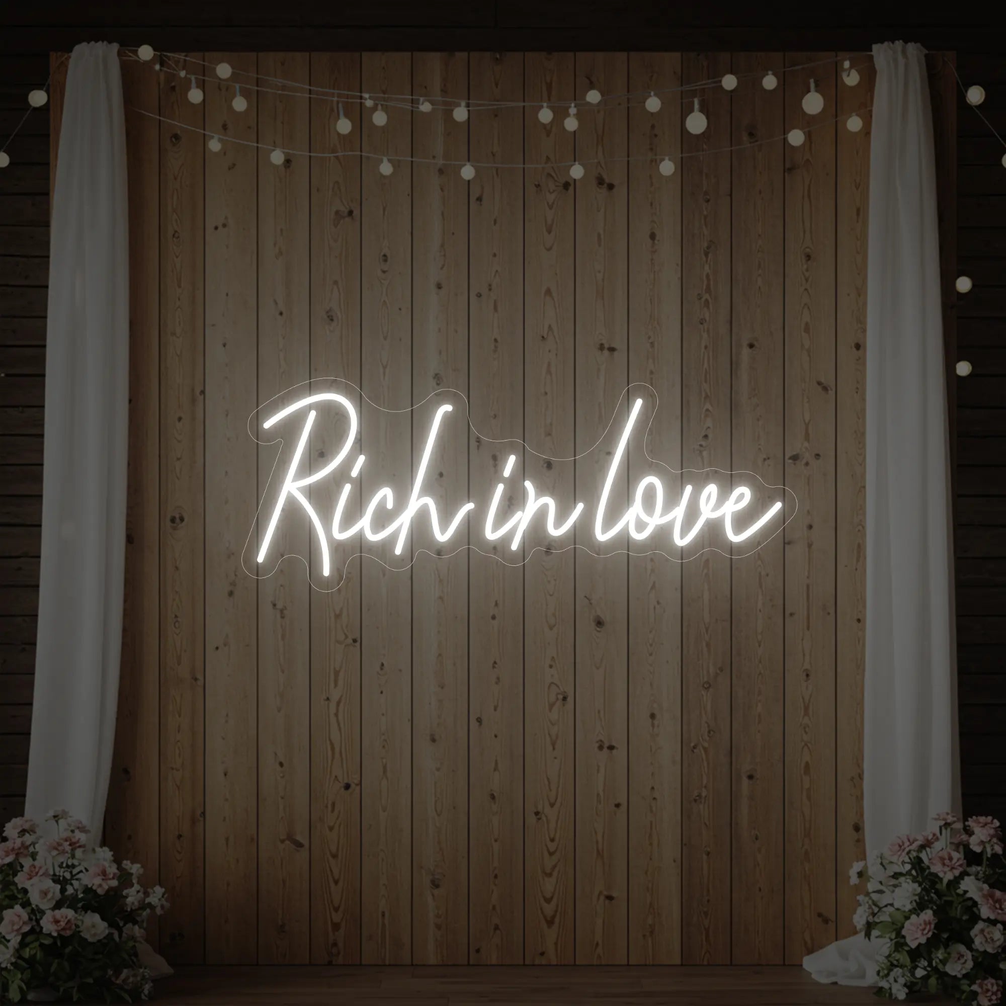 Photo of the 'Rich In Love' neon sign glowing in cool white against a styled interior wall.