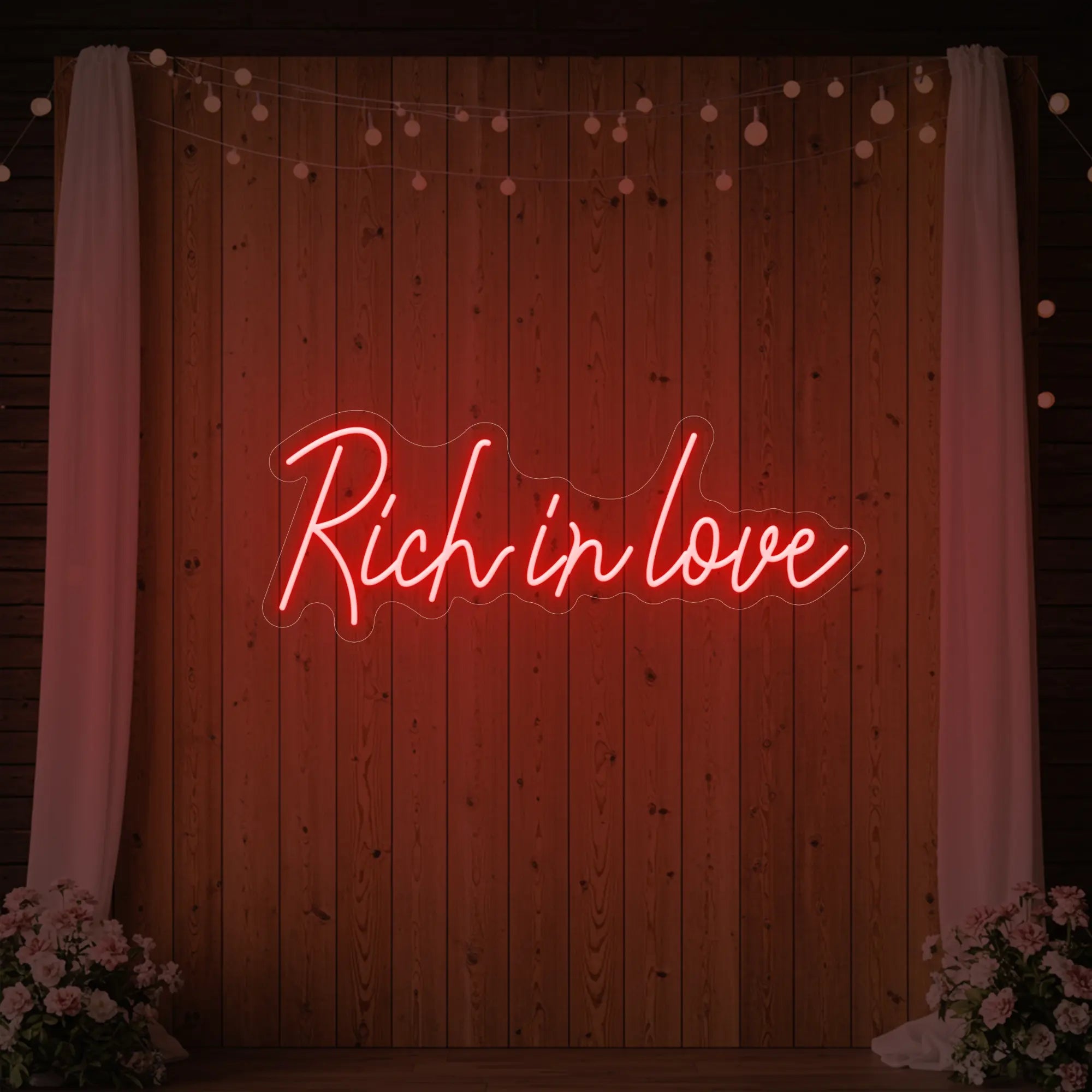Photo of the 'Rich In Love' neon sign glowing in red against a styled interior wall.