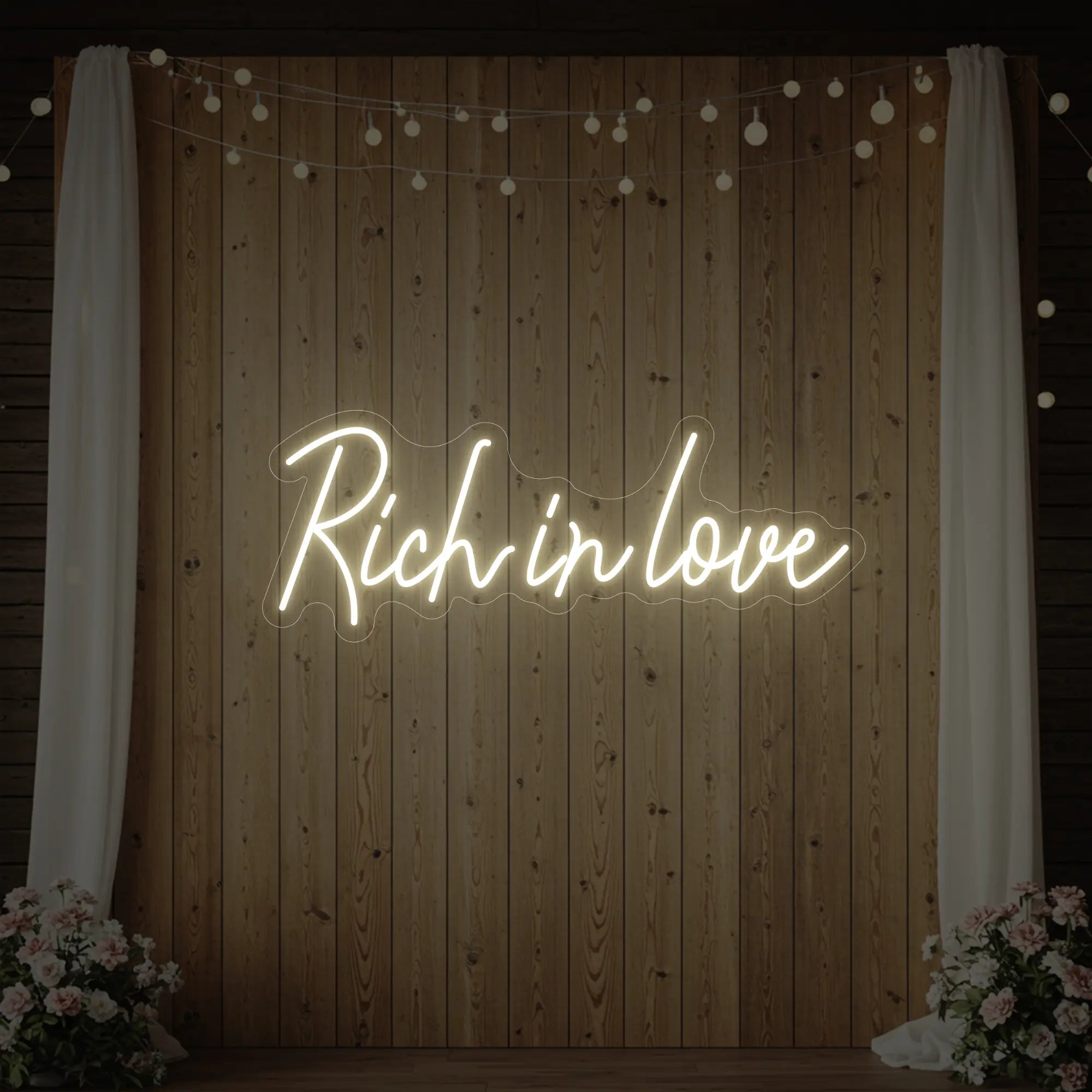 Photo of the 'Rich In Love' neon sign glowing in warm white against a styled interior wall.