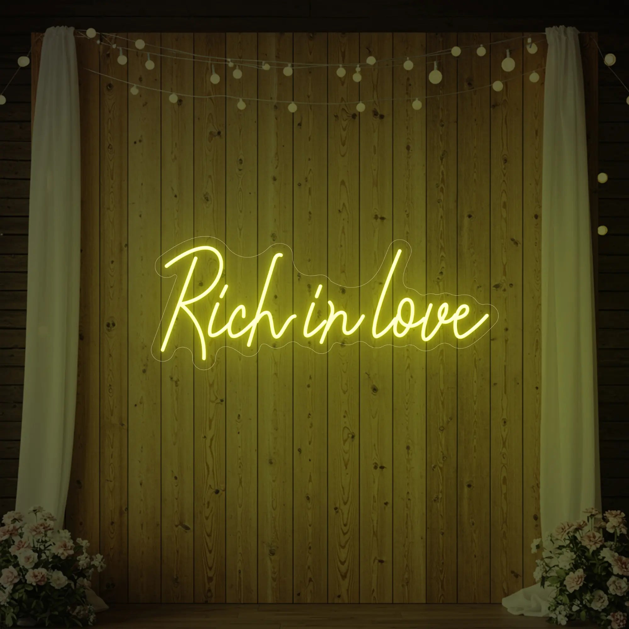 Photo of the 'Rich In Love' neon sign glowing in lemon yellow against a styled interior wall.