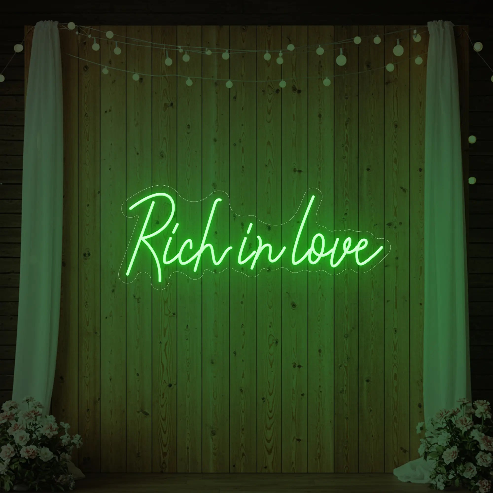 Photo of the 'Rich In Love' neon sign glowing in green against a styled interior wall.