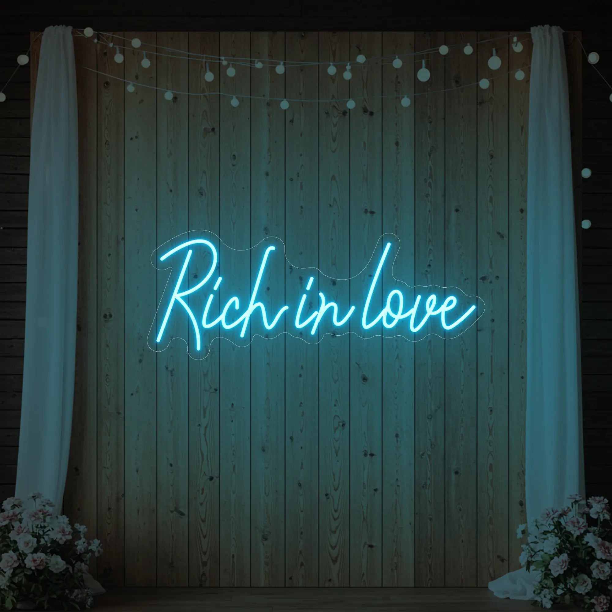 Photo of the 'Rich In Love' neon sign glowing in ice blue against a styled interior wall.