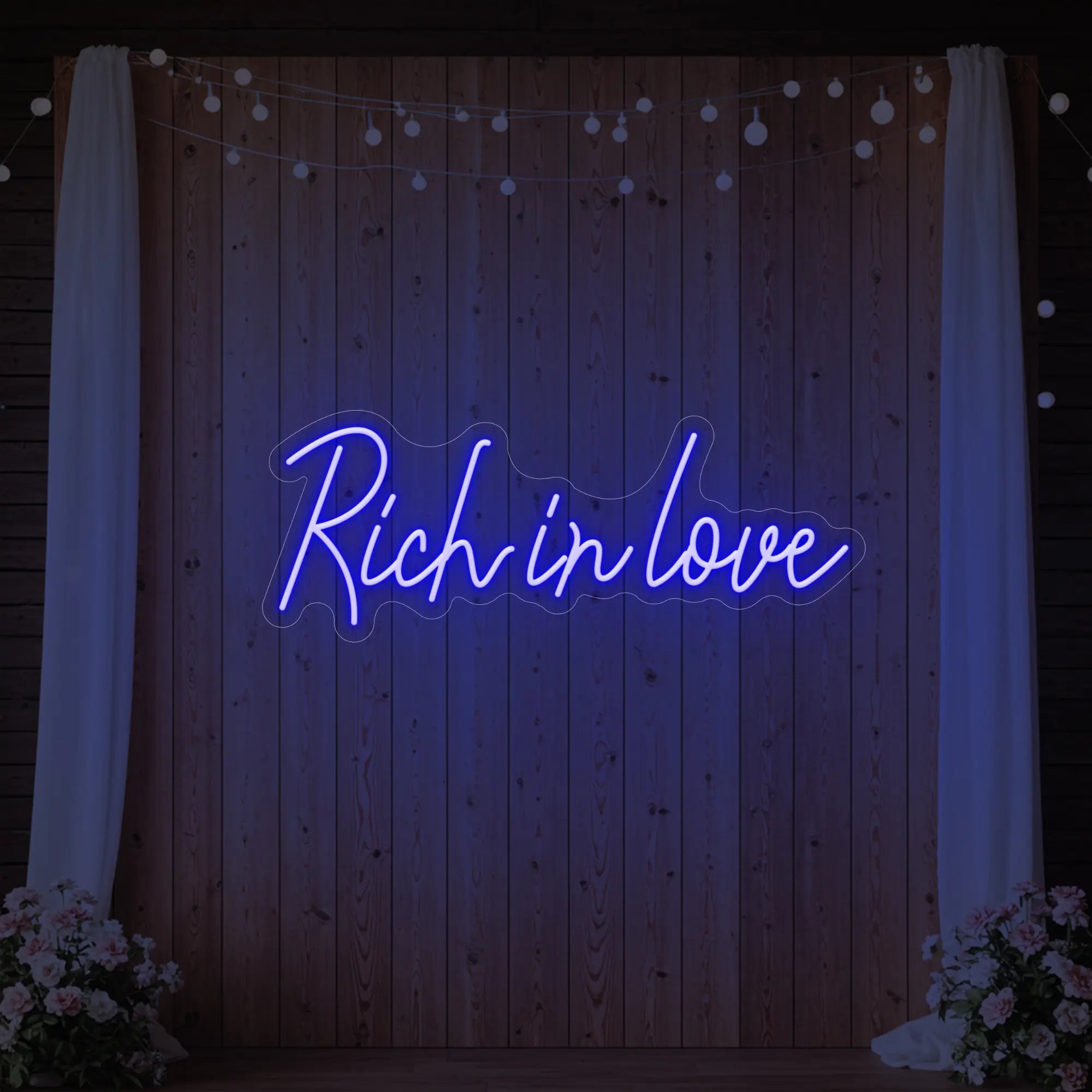 Photo of the 'Rich In Love' neon sign glowing in deep blue against a styled interior wall.