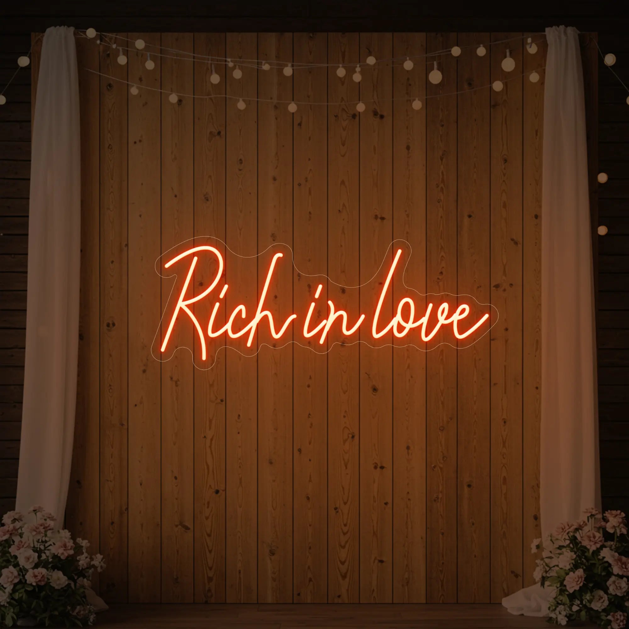 Photo of the 'Rich In Love' neon sign glowing in golden yellow against a styled interior wall.
