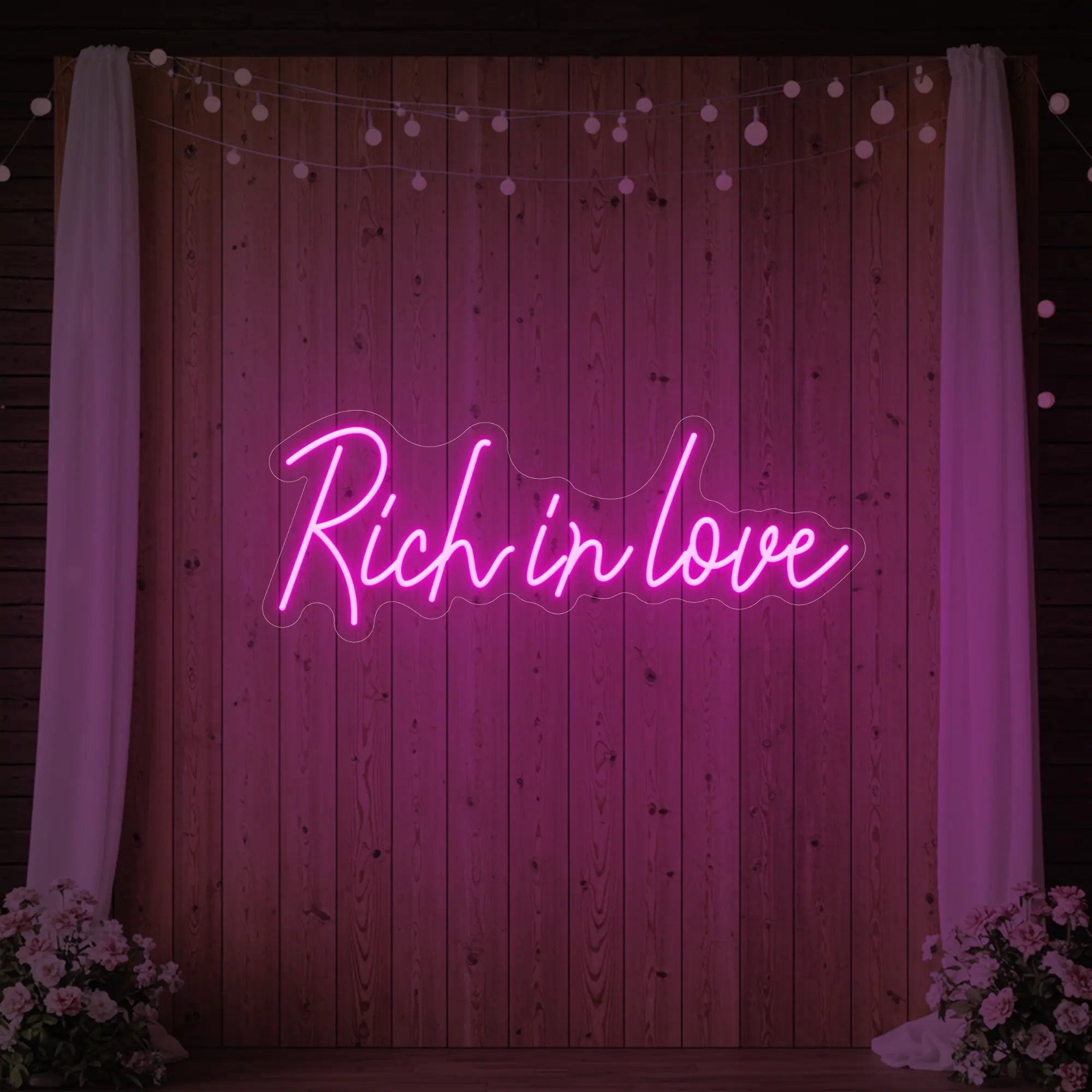 Photo of the 'Rich In Love' neon sign glowing in light pink against a styled interior wall.