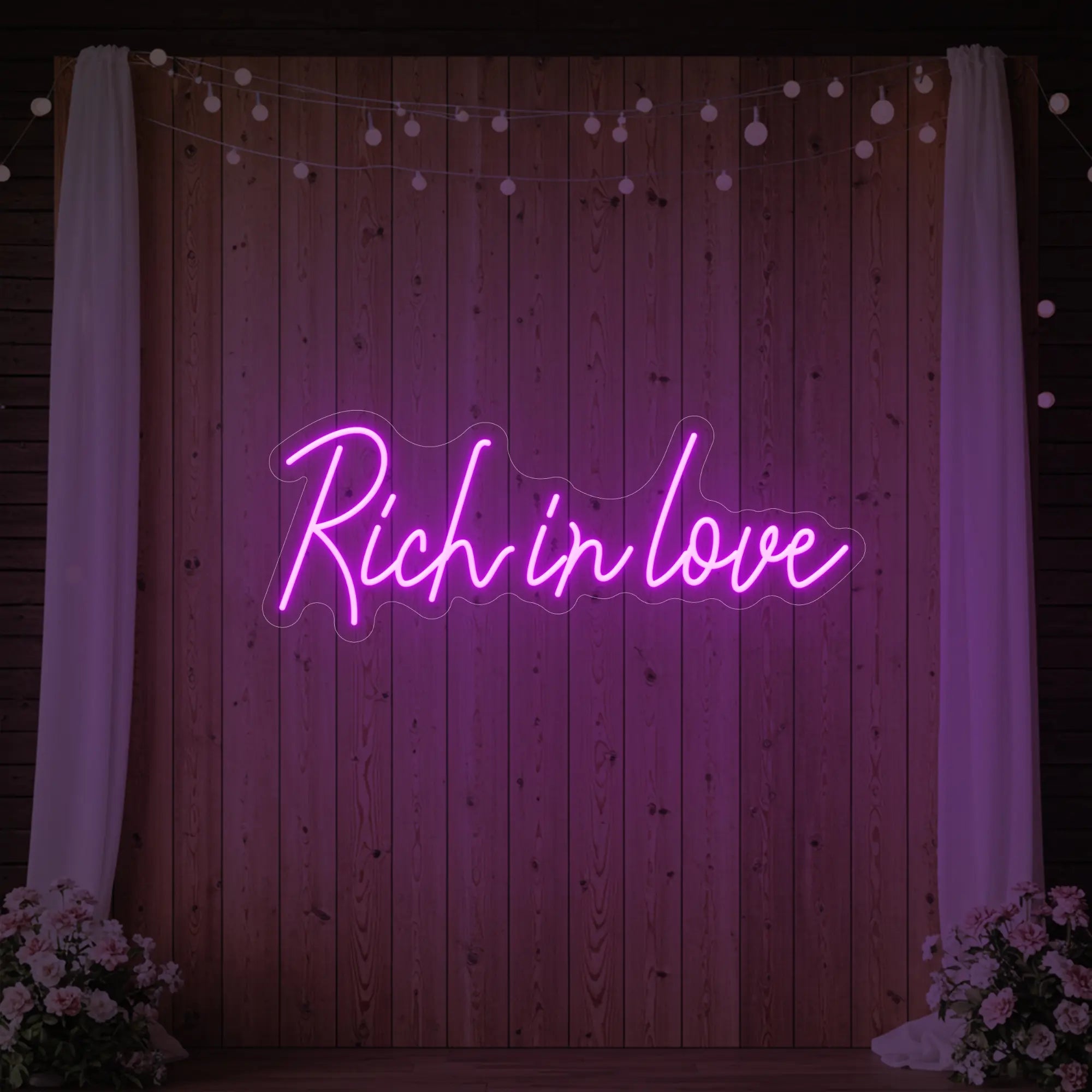 Photo of the 'Rich In Love' neon sign glowing in deep pink against a styled interior wall.