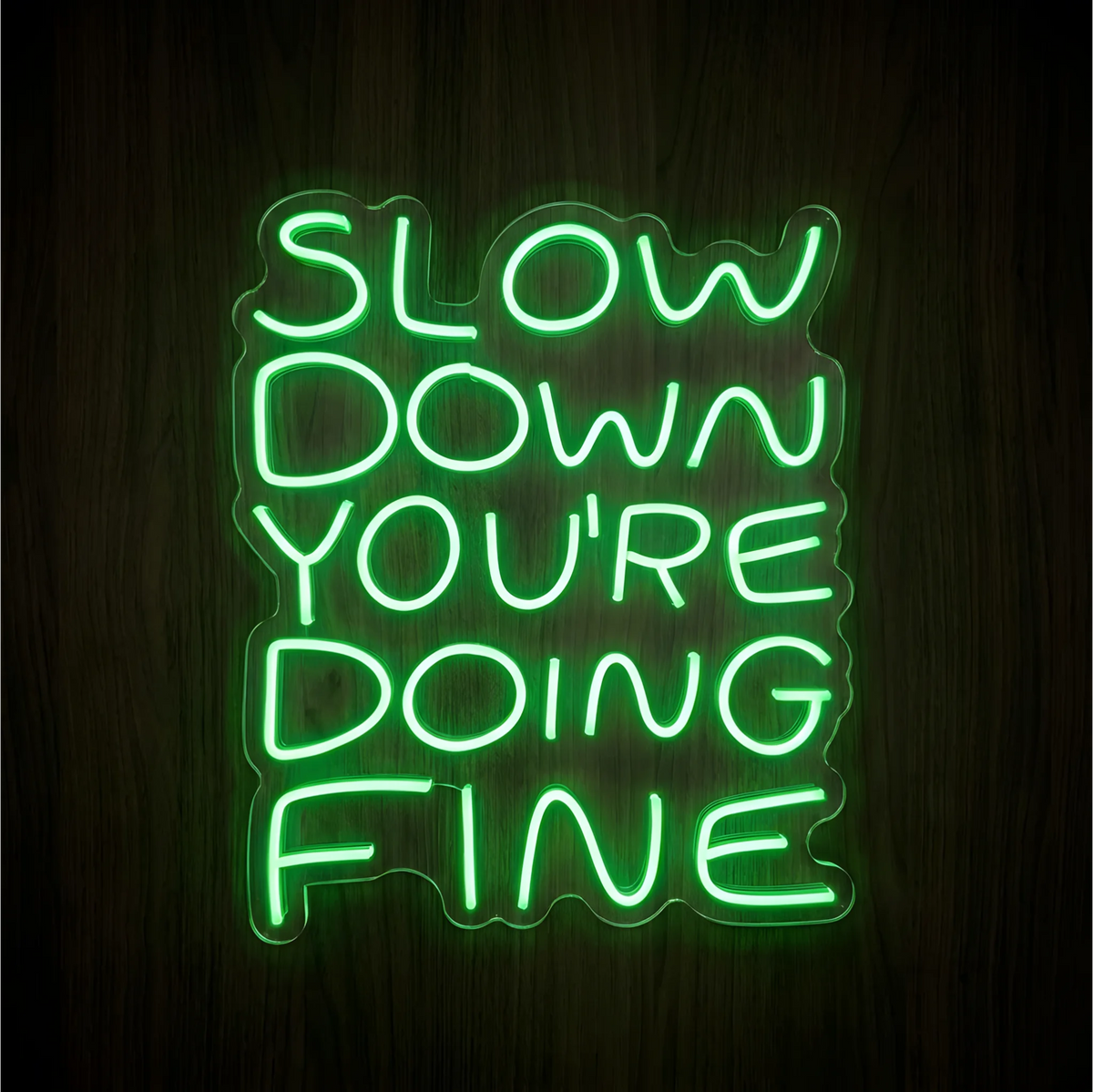 “Slow Down You’re Doing Fine” LED Neon Sign with bright green lettering on clear acrylic backing against a dark wood background, a calming accent for bedrooms and wellness spaces.