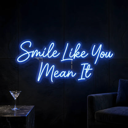 Photo of the 'Smile Like You Mean It' neon sign glowing in blue against a cozy modern interior wall.