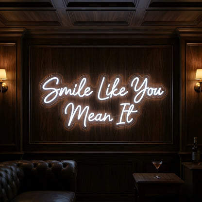 Photo of the 'Smile Like You Mean It' neon sign glowing in cool white against a cozy modern interior wall.