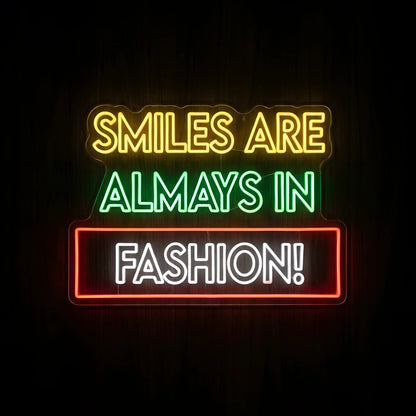 Smiles Are Always in Fashion LED neon sign featuring yellow, green, and white quote lettering with a red rectangular border on clear acrylic backing for dental clinic wall decor.