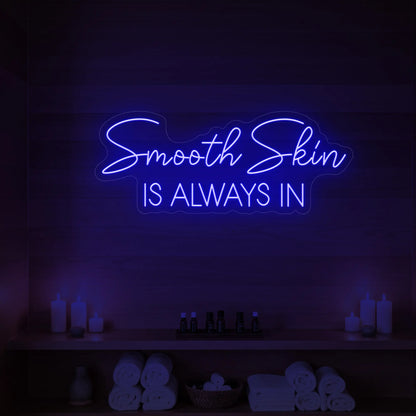 Photo of the 'Smooth Skin Is Always In' neon sign glowing in deep blue against a styled interior wall.