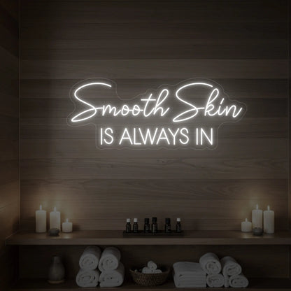Photo of the 'Smooth Skin Is Always In' neon sign glowing in cool white against a styled interior wall.

