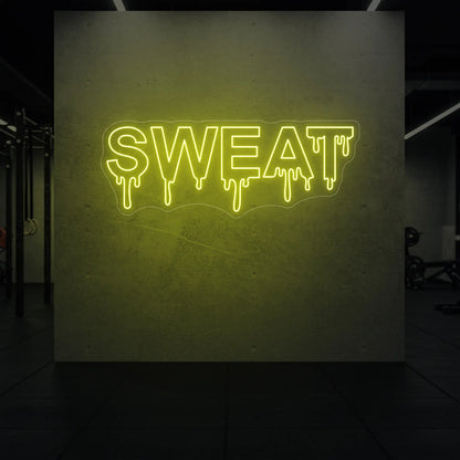 'SWEAT' neon sign glowing in lemon yellow against a styled interior wall.