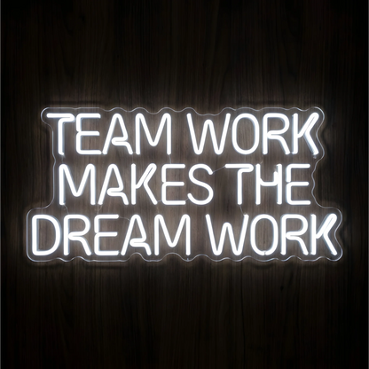Teamwork Makes the Dream Work LED Neon Sign with bright white uppercase lettering across three lines on clear acrylic against a dark wood background, ideal for offices and collaborative workspaces.