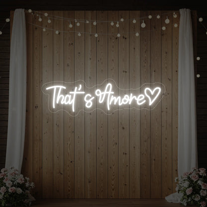Photo of the 'That's Amore with Heart' neon sign glowing in cool white against a styled interior wall.