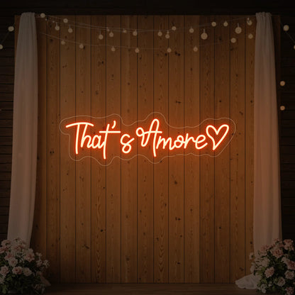 Photo of the 'That's Amore with Heart' neon sign glowing in golden yellow against a styled interior wall.