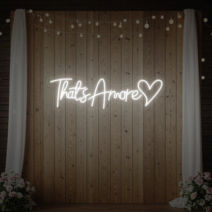 Photo of the 'That's Amore with Heart' neon sign glowing in cool white against a styled interior wall.