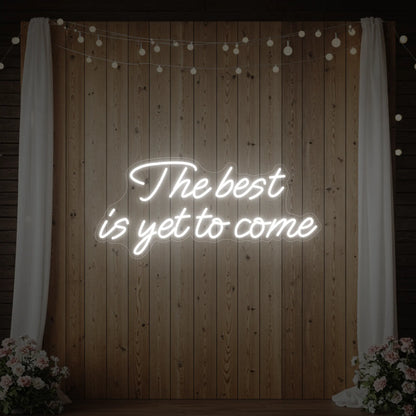 'The Best Is Yet To Come' neon sign glowing in cool white against a styled interior wall.