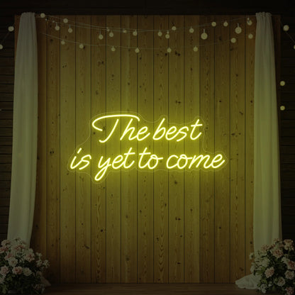 'The Best Is Yet To Come' neon sign glowing in lemon yellow against a styled interior wall.