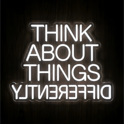 Think About Things Differently LED Neon Sign in bright white uppercase lettering on clear acrylic against a dark wood background, suited to creative studios and home offices.