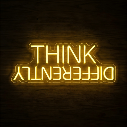 Think Differently LED Neon Sign with bright yellow uppercase lettering on clear acrylic against a dark wood background, suited to creative studios and home offices.