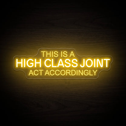 This Is A High Class Joint Act Accordingly LED neon sign with bold yellow typography mounted on a clear acrylic backing.