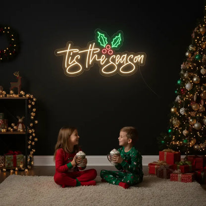 Photo of the 'Tis The Season With Mistletoe' neon sign glowing in multicolor against a styled interior wall.