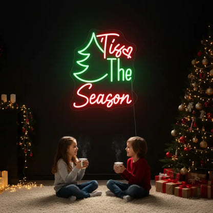 Photo of the ‘Tis The Season with Pine Tree’ neon sign glowing in multicolor against a styled interior wall.