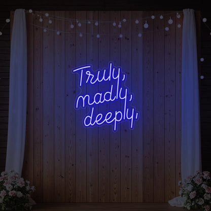  'Truly, Madly, Deeply' neon sign glowing in deep blue against a styled interior wall.