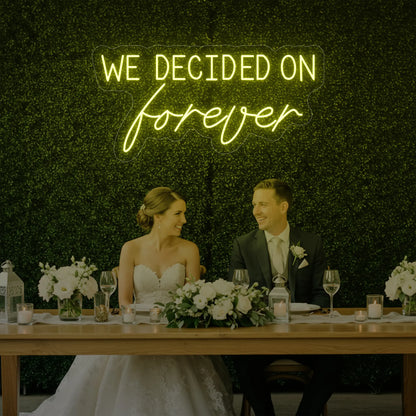  'We Decided On Forever' neon sign glowing in lemon yellow against a styled interior wall.