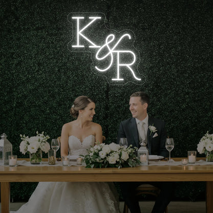 Photo of the 'Wedding Initials Custom Neon Sign V2' neon sign glowing in cool white against a styled interior wall.