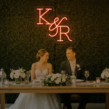 Photo of the 'Wedding Initials Custom Neon Sign V2' neon sign glowing in golden yellow against a styled interior wall.