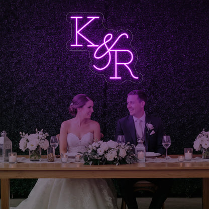 Photo of the 'Wedding Initials Custom Neon Sign V2' neon sign glowing in deep pink against a styled interior wall.
