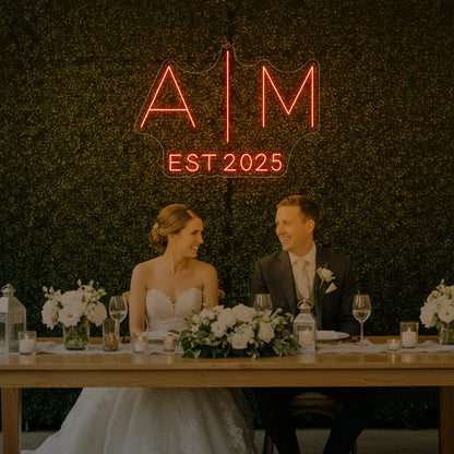 Photo of the 'Wedding Initials Custom Neon Sign V4' neon sign glowing in golden yellow against a styled interior wall.