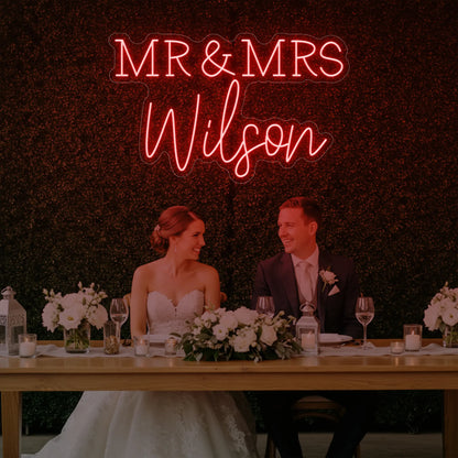 Photo of the 'Wedding Last Names Custom Neon Sign V2' neon sign glowing in red against a styled interior wall.