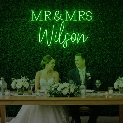 Photo of the 'Wedding Last Names Custom Neon Sign V2' neon sign glowing in green against a styled interior wall.