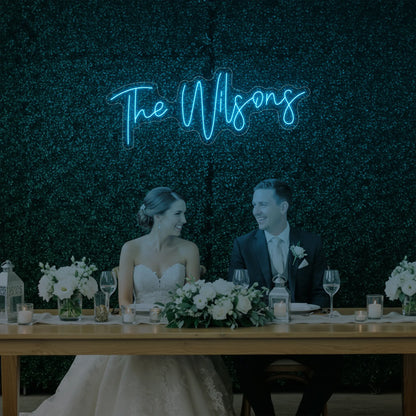 Photo of the 'Wedding Last Names Custom Neon Sign V4' neon sign glowing in ice blue against a styled interior wall.